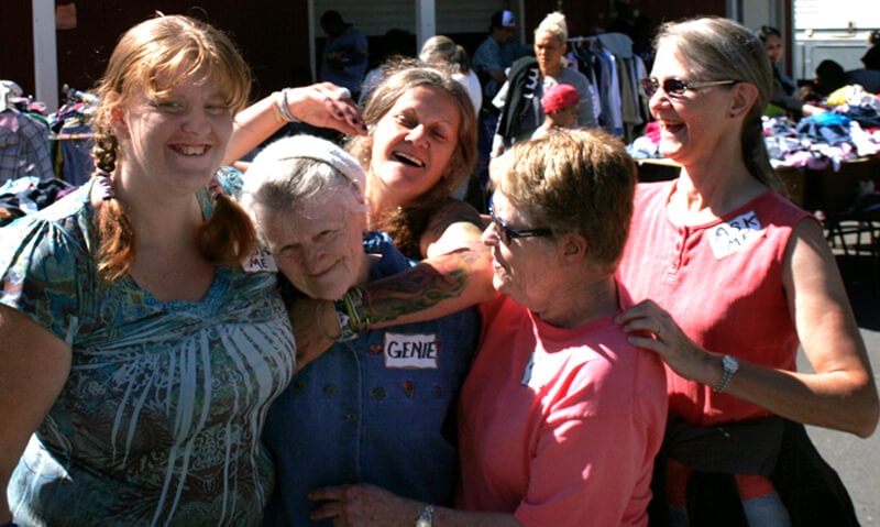 Genevieve Cochran receives love from the other event volunteers at today's Free Back to School Clothing Giveaway at the Anawim Sanctuary in Gresham. It was an event that required much planning with little time to do it. "We only had five weeks to pull this together and this couldn't have happened without my volunteers, two who are homeless" said Genevieve Cochran. Left to Right: Amber, Genevieve, Pat, Barb, Kristi